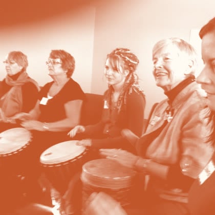 Women of different ages smiling side by side as they drum together