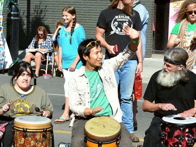 Marcus Fung facilitating a street festival drum circle, one arm raised to cue the group